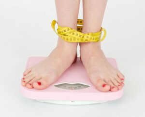 High angle of crop anonymous female with centimeter on legs checking weight on scales on white background