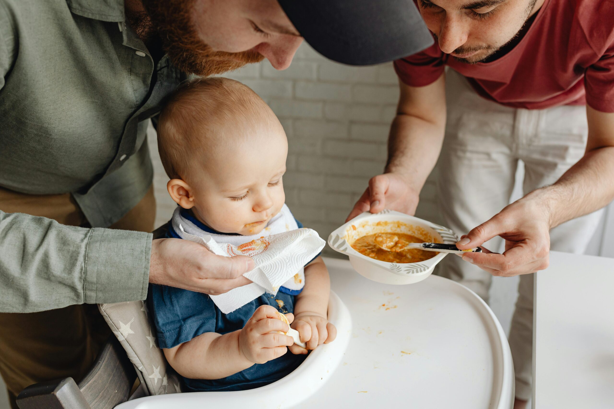 Two parents lovingly feeding their baby in a warm home environment.